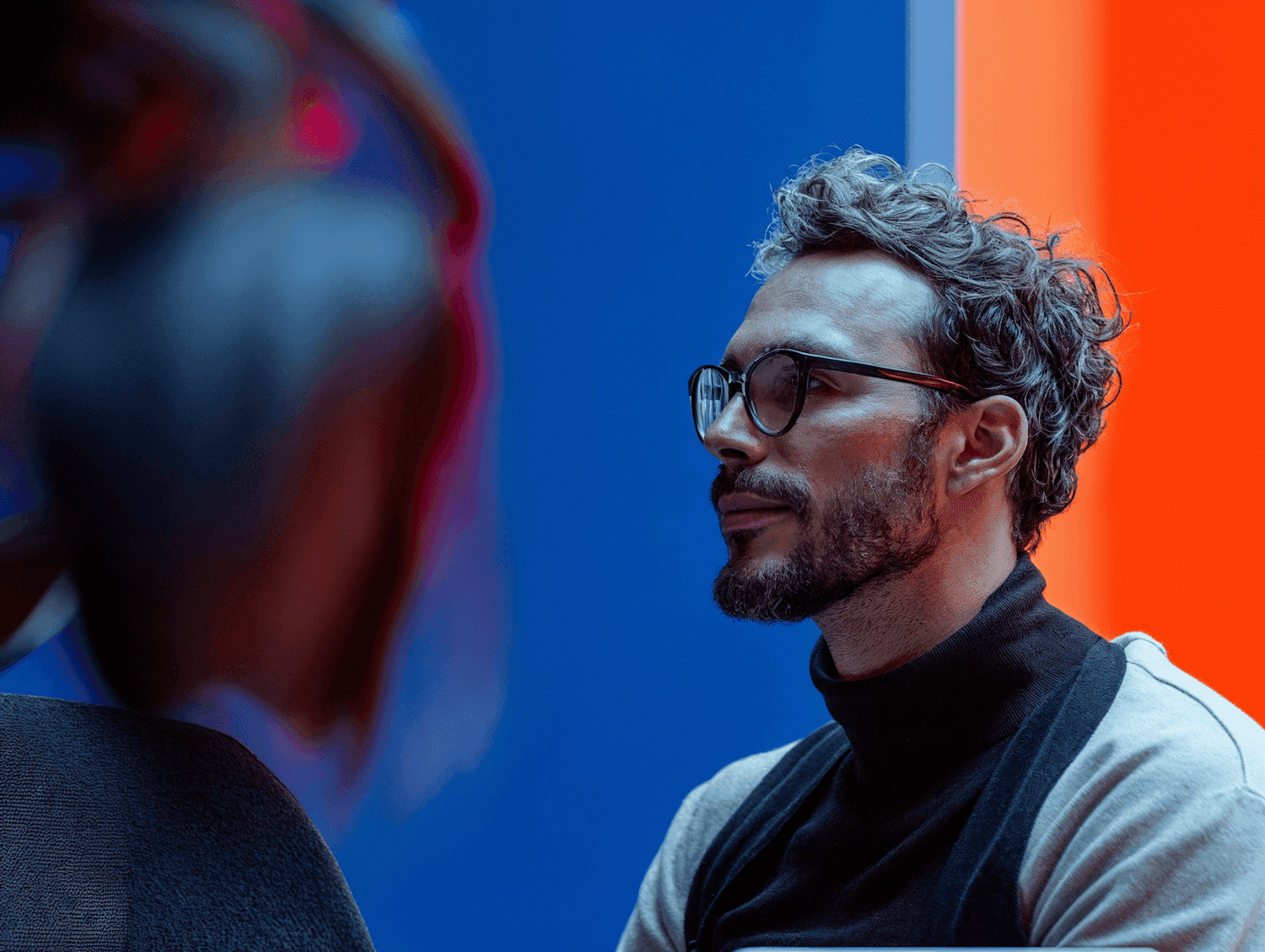 Man with glasses and grey curls against blue and orange walls